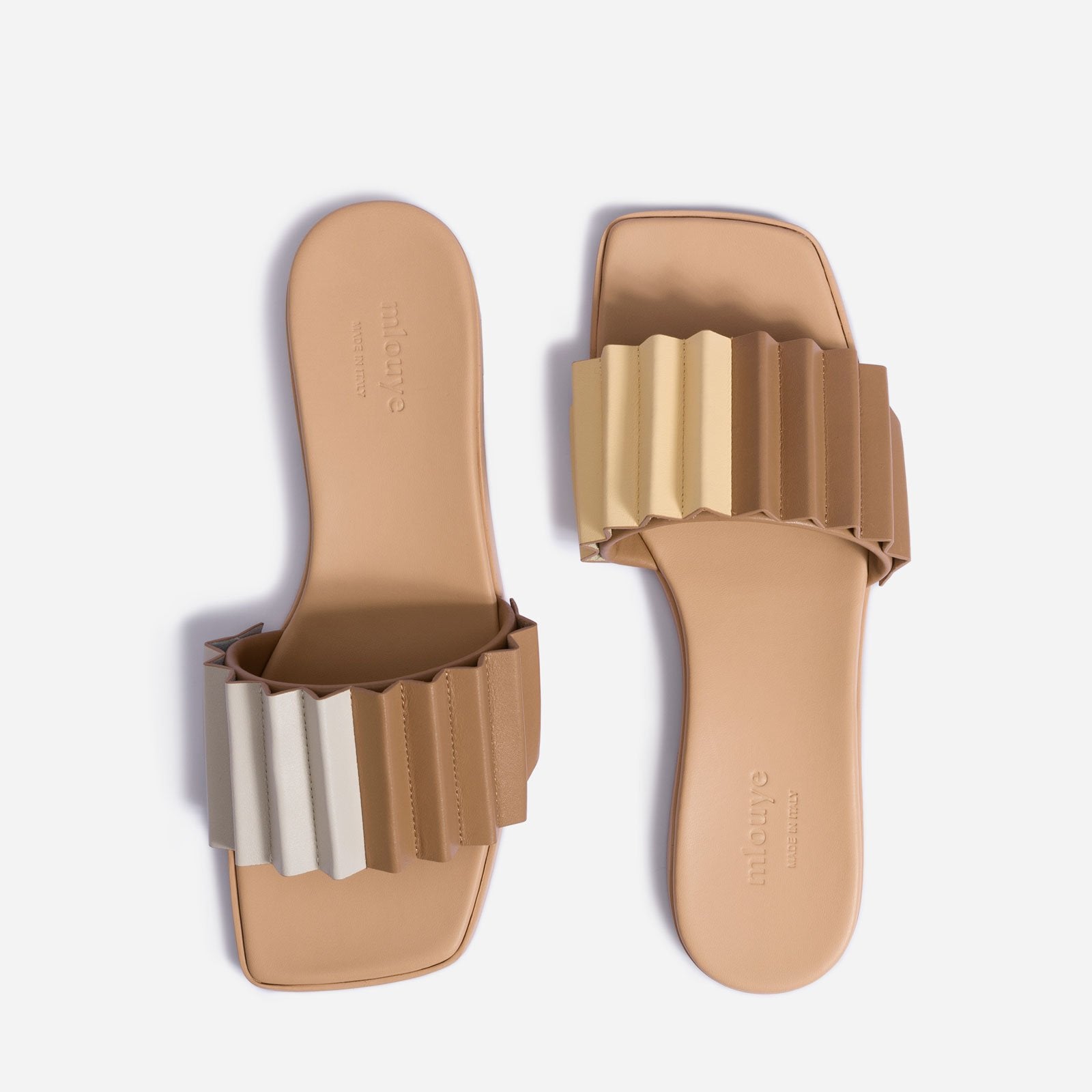 Top view of sandals, one facing up, the other facing down. Upward facing sandal strap features light cream color on left half, brown color on right half. Downward facing sandal strap features brown on left half, white on right half.